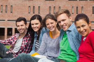 Five students sitting on the grass smiling at camera on campus at college
